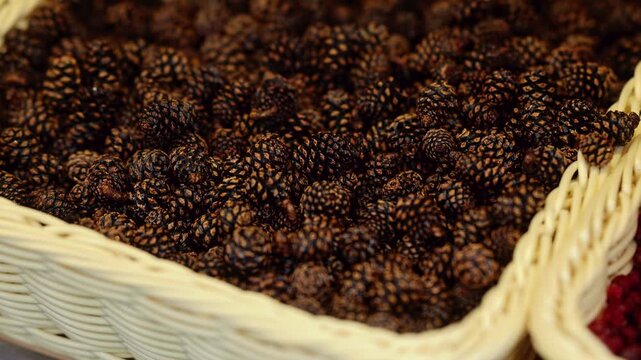 Dried alder cones in wicker basket at market stall. Natural herbal ingredients and dried plants for sale. Traditional medicine and craft materials concept.