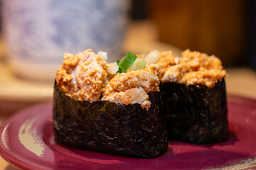 Pair of ankimo (monkfish liver) gunkan maki sushi topped with chopped green onions on a red plate. © KAI-CHIEH YANG