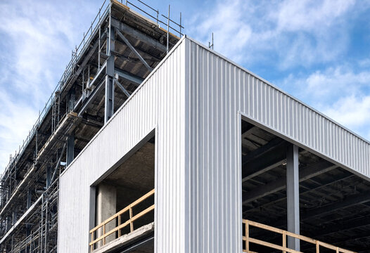 Modern industrial building under construction with metal siding and scaffolding against a blue sky