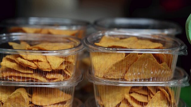 Corn tortilla chips in clear plastic containers stacked on shop shelf. Crispy nachos snack packaged for sale in store. Fast food take away concept.