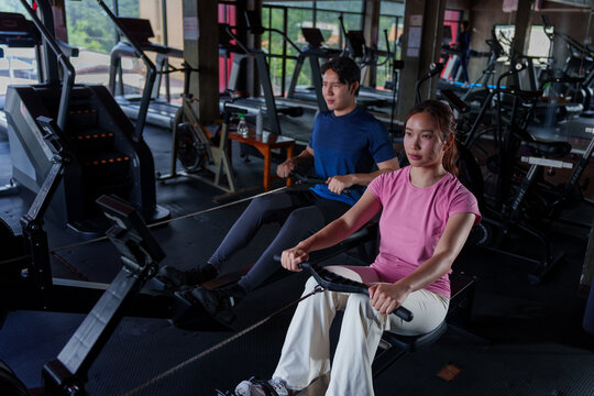 Young Asian personal trainer instructing Caucasian woman on stationary bike technique at modern fitness gym