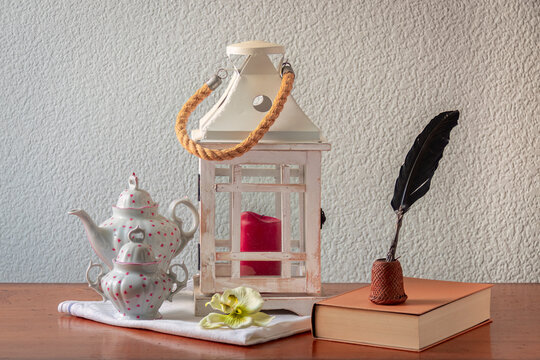 bodeg&oacute;n de un farol con vela, tetera, azucarero, pluma y un libro