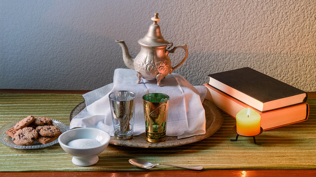 tetera arabe con vasos de te, galletas una vela y libros