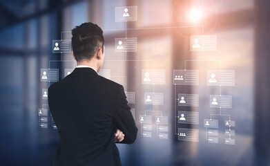 Fototapeta premium A business professional stands in a modern office, analyzing an organizational chart displayed on a digital interface, embodying analysis, strategy, and teamwork. Ledger