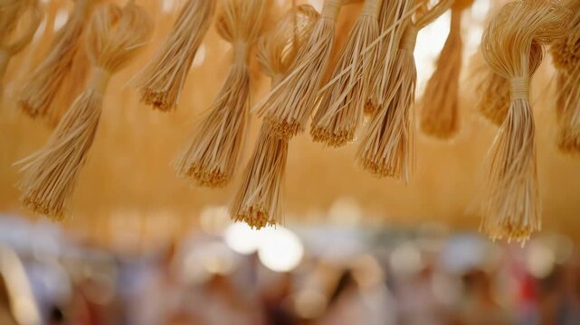 Hanging bundles of pale fiber tassels sway gently in warm backlight above a softly blurred crowd, revealing fine strands, tied loops, layered texture, and shallow focus