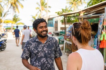 Naklejka premium Begegnung mit einem Einheimischen auf den Malediven: Eine Urlauberin unterhält sich in einer belebten Inselstraße mit einem freundlichen Bewohner nahe dem tropischen Strand.