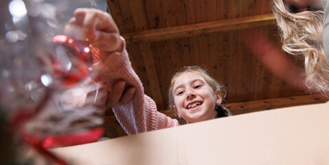 Obraz premium A girl smiles as she takes a Christmas ornament out of a box