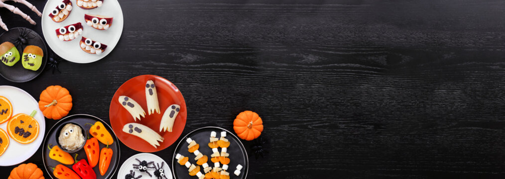 Healthy Halloween fruit and vegetable snacks. Variety of fun, spooky treats. Top view corner border over a black wood banner background with copy space.