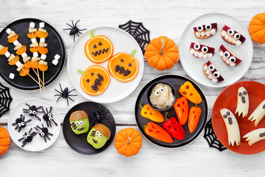 Healthy Halloween fruit and vegetable snacks. Variety of fun, spooky treats. Above view table scene over a white wood background.