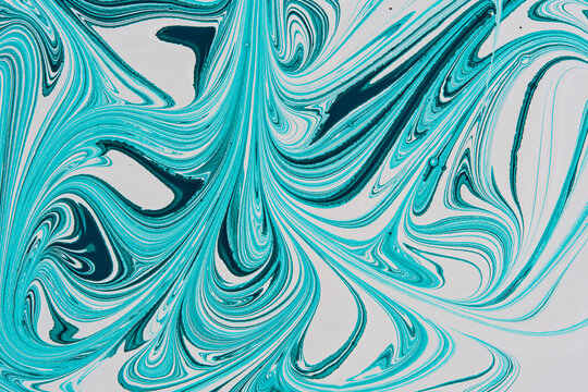Abstract ebru paint art with turquoise and dark blue swirling marble patterns on white background.