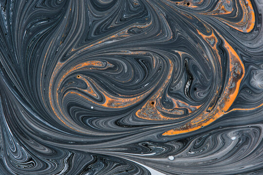 Abstract liquid paint swirl pattern featuring dark grey marble with vibrant orange accent lines.