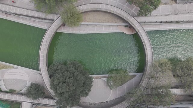 Aerial top-down view of the circular bridge over the Paseo Santa Luc&iacute;a canal in Monterrey as water flows and a person walks by, Nuevo Le&oacute;n. D-Log M