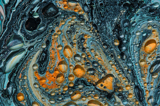 Top view macro pattern swirling dark blue, orange, and white fluid paint with circular cells.