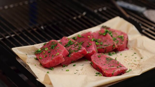 Raw tuna steaks with fresh herbs on parchment paper over grill grate. Fresh fish fillets seasoned with dill prepared for barbecue cooking. Seafood gourmet cuisine concept.