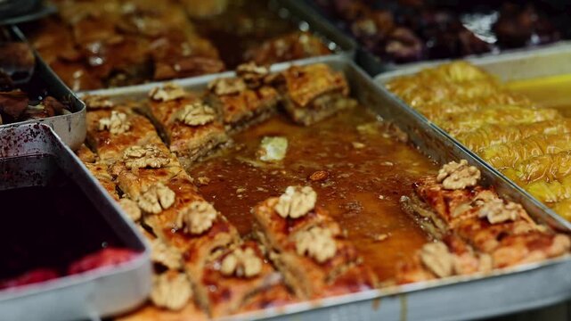 Traditional baklava with walnuts in metal tray at oriental sweets market. Turkish dessert stall with honey pastry, syrup and assorted confectionery. Middle eastern street food concept.