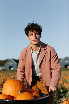 Young man in pumpkin patch autumn portrait with wheelbarrow for seasonal banner background and fall harvest marketing use