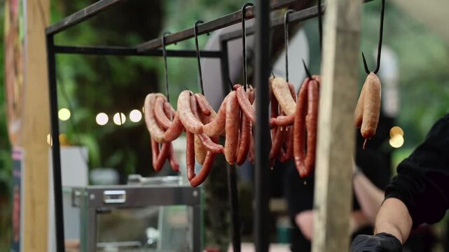 Sausages hanging on hooks at outdoor christmas market stall. Traditional smoked sausages for sale on street food festival. Festive winter holiday market food concept