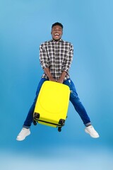 Happy Smiling Black Male Traveler Jumping With Yellow Suitcase In Bright Studio Setting, Showing...