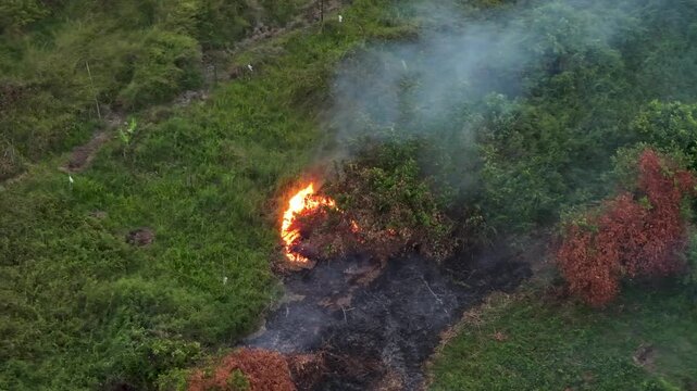 Thick grey smoke rises from a patch of dry grass and bushes burning in a grassy field