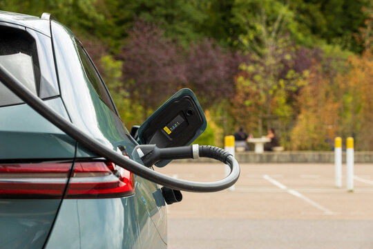 Electric vehicle plugged into a power charger with passengers resting at a picnic table in the blurred background