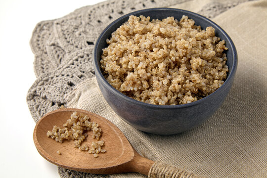 boiled quinoa in a gray ceramic bowl and a wooden spoon on a beige linen patterned tablecloth