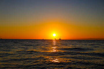 Obraz premium Orange sky on the sunset at the sea, lake. Evening sea horizon. Tranquil ships, boats and people silhouettes at sea during a colourful sunset. Travel, touristic, vacation concept. Tour touristic 