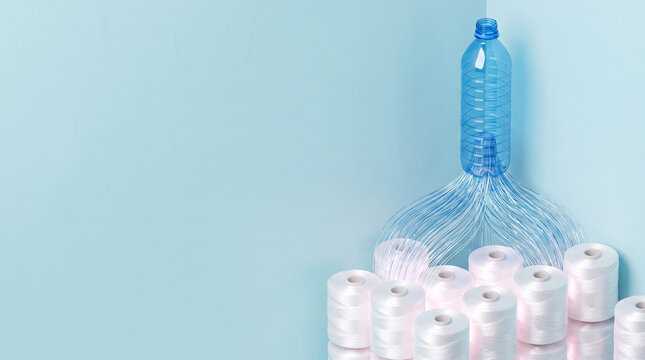 Recycled PET plastic bottle transforming into white polyester thread spools, symbolizing circular economy and sustainable textile fiber recycling, light blue background with copy space