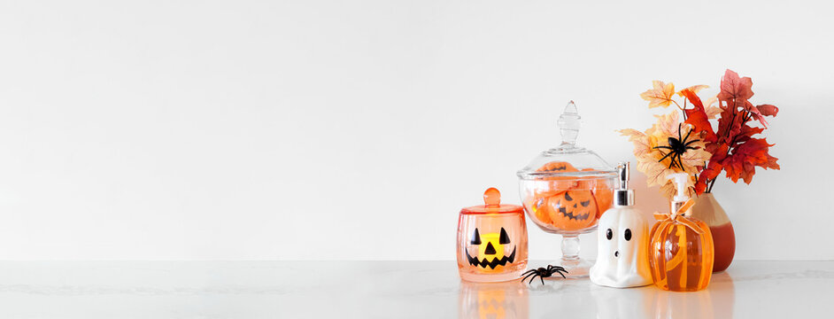 Halloween pumpkin and ghost theme body care on a white stone countertop. Banner against a white wall background with copy space. Bathroom decor concept. Soaps, lotion, bath fizzers.