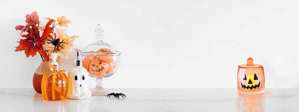 Halloween pumpkin and ghost theme body care on a white stone countertop. Banner against a white wall background with copy space. Bathroom decor concept. Soaps, lotion, bath fizzers.