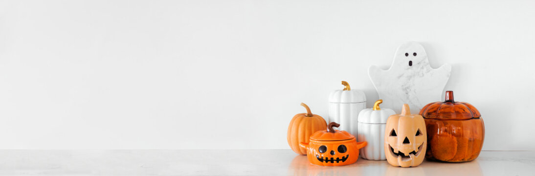 Halloween ghost and pumpkin theme kitchenware on a white stone countertop. Banner against a white wall background with copy space. Autumn kitchen decor concept.