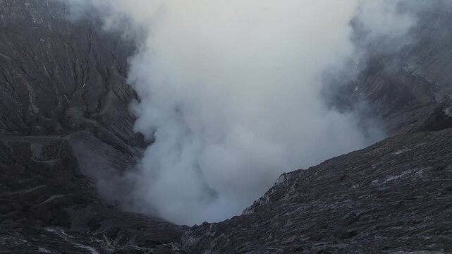 Man and woman hiking on the edge of an active volcano crater looking at the erupting smoke