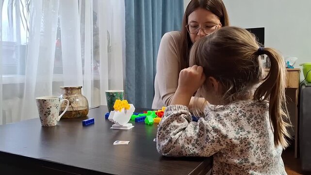 Mother and daughter play with colorful building blocks at home in the afternoon