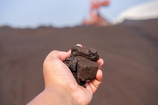 Hand holding a handfull of coal dark soil samples, industrial background, close-up