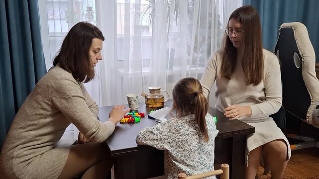 Two women interact with a young girl at a table during an indoor activity