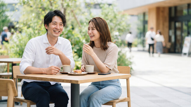 カフェのオープンテラスで笑顔で会話を楽しむ若い夫婦