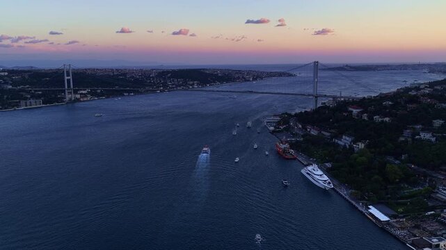 Aerial cityscape of Istanbul Bosphorus shoreline featuring waterfront estates, boats, deep blue sea, and green hills under clear sky