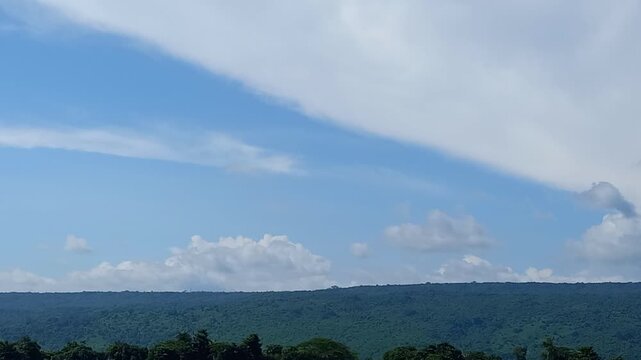 Rolling green hills under a vast blue sky with dynamic cloud formations during daylight
