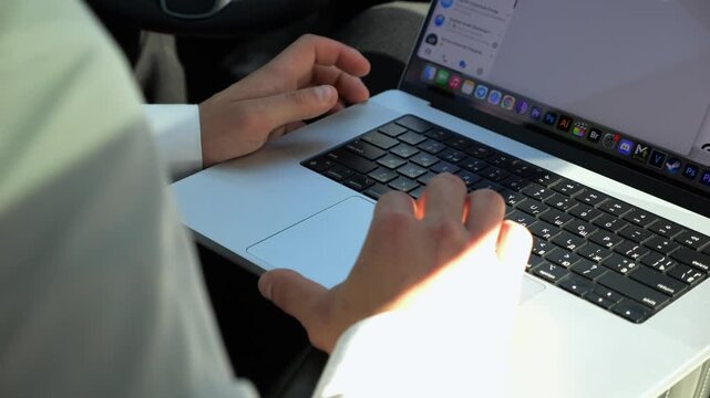 Male hands of entrepreneur typing text on laptop while riding in autonomous self-driving electric car on urban road. Businessman work on notebook during trip in automated eco vehicle with autopilot