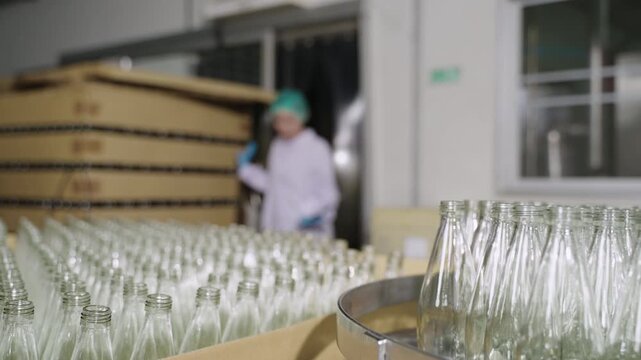 Professional Asian woman inspector worker in uniform of beverage factory holding and using digital tablet for analysis and checking the quality of empty glass bottles in the industry production line. 