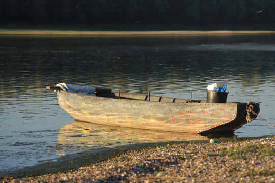 Old weathered metal fishing boat with rusted rivets moored on the Danube riverbank in golden evening light