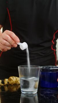 Sportsman pours scoop of supplement powder into glass of water in home kitchen. Concept of mixing electrolytes isotonic creatine glutamine bcaa slimming drink for fitness energy and muscle recovery