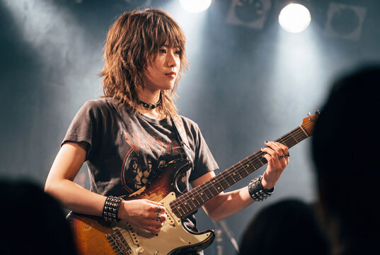 ライブハウスのステージでエレキギターを真剣に弾く女性ミュージシャン