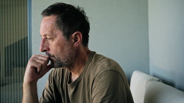 Pensive middle-aged man sitting on sofa deep in thought looking worried and contemplative, 4K