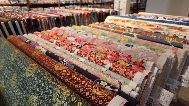 Assorted patterned fabric bolts with floral and geometric prints displayed on slanted shelves for quilting material and textile design background