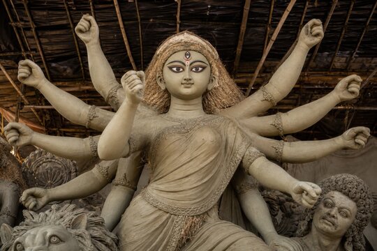 Clay Durga idol with multiple arms raised in defiance during preparation for festival