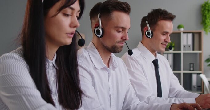 Customer support operators in headsets work in a callcenter using laptops in an office, delivering service, helpdesk aid, and teamwork for customers. Three agents collaborate at modern desks.