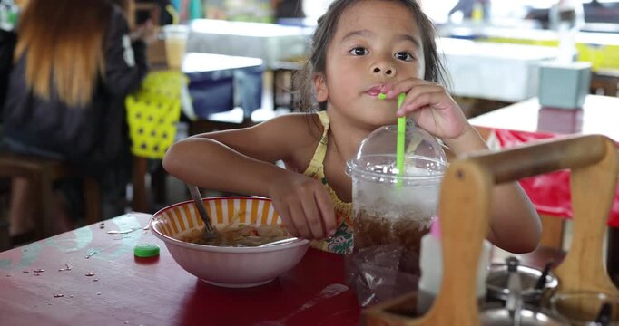 Adorable kindergarten kid girl eat noodle street food floating market Thailand