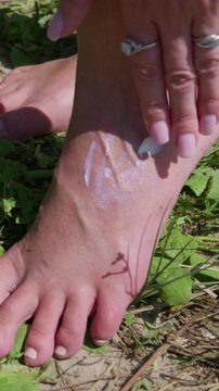 A female hand with pink manicured nails gently rests on a bare foot outdoors. Concept of foot care, natural body skincare routines, barefoot relaxation, and outdoor wellness.