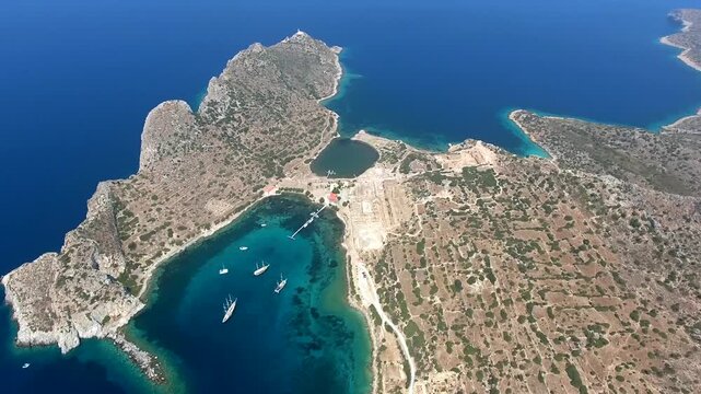 Yachts rest in a turquoise bay at Knidos, Datca, where rocky shores frame clear coastal water. Anchored sailboats and sheltered cove create a tranquil Aegean scene with charter travel appeal.