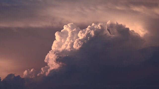 Cumulonimbus tower rises at sunset, building a dense thunderstorm beneath glowing evening sky. Rolling raincloud and severe atmosphere create a powerful weather scene with dramatic cloud mass.